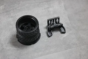 A black 3D-printed RC transmitter steering wheel assembly and a separate mounting bracket on a grey surface.