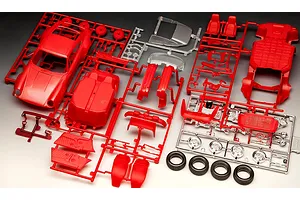 Plastic model kit parts for a 1975 Porsche 911 Turbo, including red car body, chassis, interior, chrome wheels, and black rubber tires on sprues.