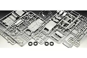 Unassembled plastic model kit parts for a 1/24 scale VW Golf 1, including grey sprues with car body, interior, and chassis components, plus four black rubber tires.