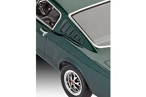A close-up view of a dark green 1965 Ford Mustang 2+2 Fastback model car showing the rear quarter panel, side window louvers, and wheel.