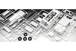 Unassembled white plastic model kit parts for a VW T3 bus on sprues with black rubber tires.