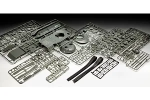 A collection of grey plastic model tank parts on sprues and two black rubber tank tracks laid out on a white surface.