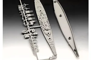Unassembled grey plastic model kit parts for a battleship, including a sprue with turrets and the ship's deck and hull pieces.