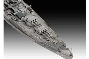 A high-angle close-up view of the bow section of a grey plastic model battleship, showing the deck, gun turrets, and anchor chains.