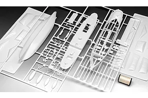 White plastic model kit sprues for a ship model, including hull sections and deck parts, laid out on a flat surface with a spool of thread.