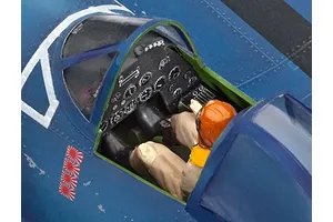 Close-up of a painted plastic model aircraft cockpit with a pilot figure seated inside, showing detailed instrument panel and blue fuselage.