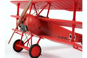 A close-up, side-angle view of a red Fokker DR.1 triplane plastic model aircraft on a white background.