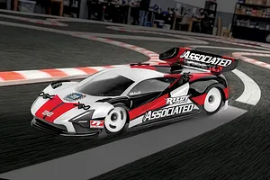 A Team Associated TC28 RC touring car driving on an indoor carpet race track with red and white curbing.