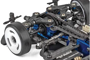 Close-up of the chassis and suspension components of a Team Associated RC car, showing blue anodized aluminum parts, a drive belt, and rubber tires.