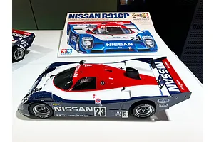 A Tamiya Nissan R91CP 1/10 scale RC car kit box and a fully assembled model car on a white surface.