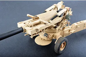 A high-angle studio shot of a 1/16 scale M198 155mm towed howitzer plastic model kit, painted in a desert tan camouflage scheme.