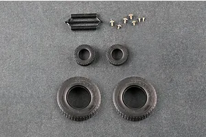 A top-down view of model kit parts including two large rubber tires, two small rubber tires, a black plastic spring assembly, and several small metal screws.