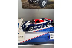 A Tamiya 1/10 scale Nissan R91CP RC car model on display at a hobby show with red, white, and blue racing livery.