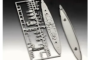 Grey plastic model kit parts for a battleship, including a sprue frame with turrets and the ship's deck and hull pieces.