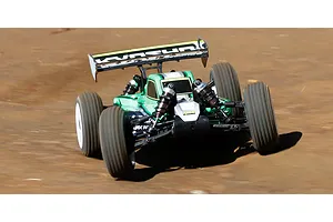 A green Kyosho Inferno MP10e RC buggy driving on a dirt track, showing its rear wing and suspension.