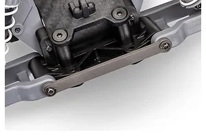Close-up of the front suspension assembly on a Traxxas RC vehicle, showing the grey plastic control arms, black chassis components, and a metal tie bar.