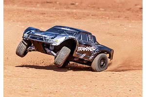 A black Traxxas Slash RC short course truck driving on a dirt track, kicking up dust with its rear wheels while cornering.