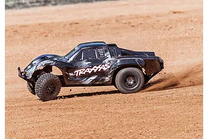 A black Traxxas Slash RC short course truck driving on a dirt track, kicking up dust.