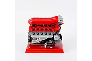 A side view of the Teching DM108 V12 engine model kit, featuring red intake manifolds and a silver engine block mounted on a red wooden base.