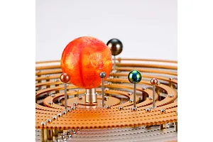 A close-up view of a Teching DM405 solar system metal model kit featuring a large textured orange sun and several small metallic planets on concentric gear rings.
