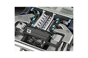 Close-up of a detailed scale model car engine, showing metallic components, black hoses with blue connectors, and small decals.