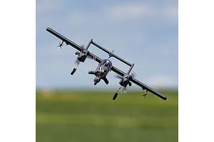 An E-Flite Micro OV-10 Bronco RC plane flying in the air with a blurred green field and blue sky background.