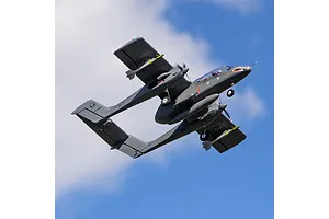 An E-Flite Micro OV-10 Bronco RC plane flying against a blue sky with white clouds.