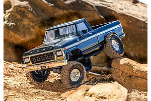 A black Traxxas TRX-4 1979 Ford F-150 Ranger XLT RC rock crawler driving over rugged rocky terrain outdoors.