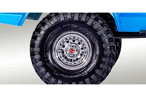 Close-up of a Traxxas RC crawler wheel with a chrome rim and black off-road tire, positioned under a blue vehicle body.