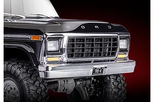 Close-up of the front grille, bumper, and hood of a black Traxxas TRX-4 1979 Ford F-150 RC crawler against a dark red background.