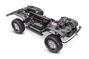 High-angle studio shot of a Traxxas TRX-4 RC crawler chassis without the body shell, showing the frame, wheels, motor, and drivetrain.
