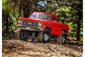 A bright red Traxxas TRX-4 1979 Chevrolet K10 RC truck driving on a dirt trail in a wooded area.