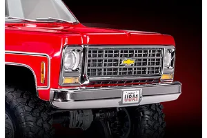 Close-up of the front end of a red Traxxas TRX-4 1979 Chevrolet Cheyenne K10 RC crawler, showing the chrome grille, headlights, and USA-1 license plate.
