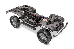 A high-angle studio shot of a Traxxas TRX-4 RC crawler chassis without the body shell, showing the frame, wheels, motor, and drivetrain components.