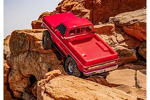 A red Traxxas TRX-4 1979 Chevrolet Cheyenne K10 RC rock crawler climbing over rugged orange rocks in an outdoor setting.