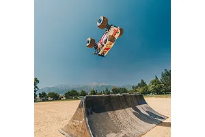An ARRMA Freedom Flyer Grom RC monster truck performing a high jump off a ramp in a park with mountains in the background.