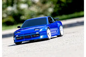 A blue Traxxas Nissan 240SX RC drift car driving on a paved surface with a blurred outdoor background.