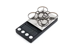 A clear grey BetaFPV drone frame sitting on a digital scale against a white background.