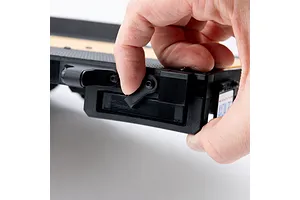 A hand adjusting a latch on the side of an Axial 1/10 scale flat bed vehicle trailer against a white background.
