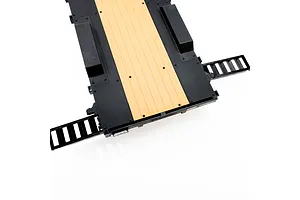 A top-down view of an Axial 1/10 scale flat bed RC vehicle trailer featuring a black diamond-plate deck with a tan wood-look center section and two fold-out ramps.