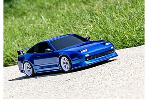 A blue Traxxas 4-Tec 2.0 Nissan 240SX RC drift car driving on a paved surface with a grassy background.