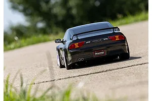 Rear view of a black Traxxas Nissan 240SX RC drift car driving on a paved road with a blurred green background.