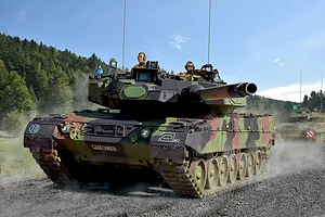 A detailed illustration of a German Leopard 2A7A1 main battle tank moving along a dirt road with crew members visible in the turret.