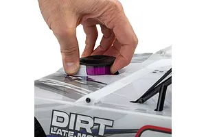 A person's hand installing a black and purple air filter cover onto the white body of a Losi 22S Dirt Late Model RC car.
