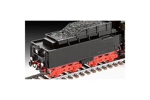 A close-up view of a black and red model steam locomotive tender sitting on grey plastic train tracks.