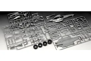 Silver plastic model kit sprues for a Formula 1 race car, including body panels, wheels, and chassis parts, laid out on a white surface.