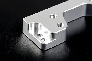Close-up of a silver Rovan aluminium engine mount showing machined edges and threaded screw holes against a black background.