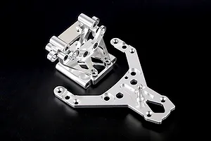 A silver aluminium front bulkhead assembly and matching upper plate for an RC vehicle, shown against a plain black background.
