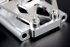 Close-up of a silver aluminium RC front bulkhead set with an upper plate against a dark background.
