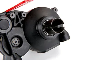Close-up of a black plastic RC transmission gear case assembly with a metal drive cup and red anodized aluminum component.